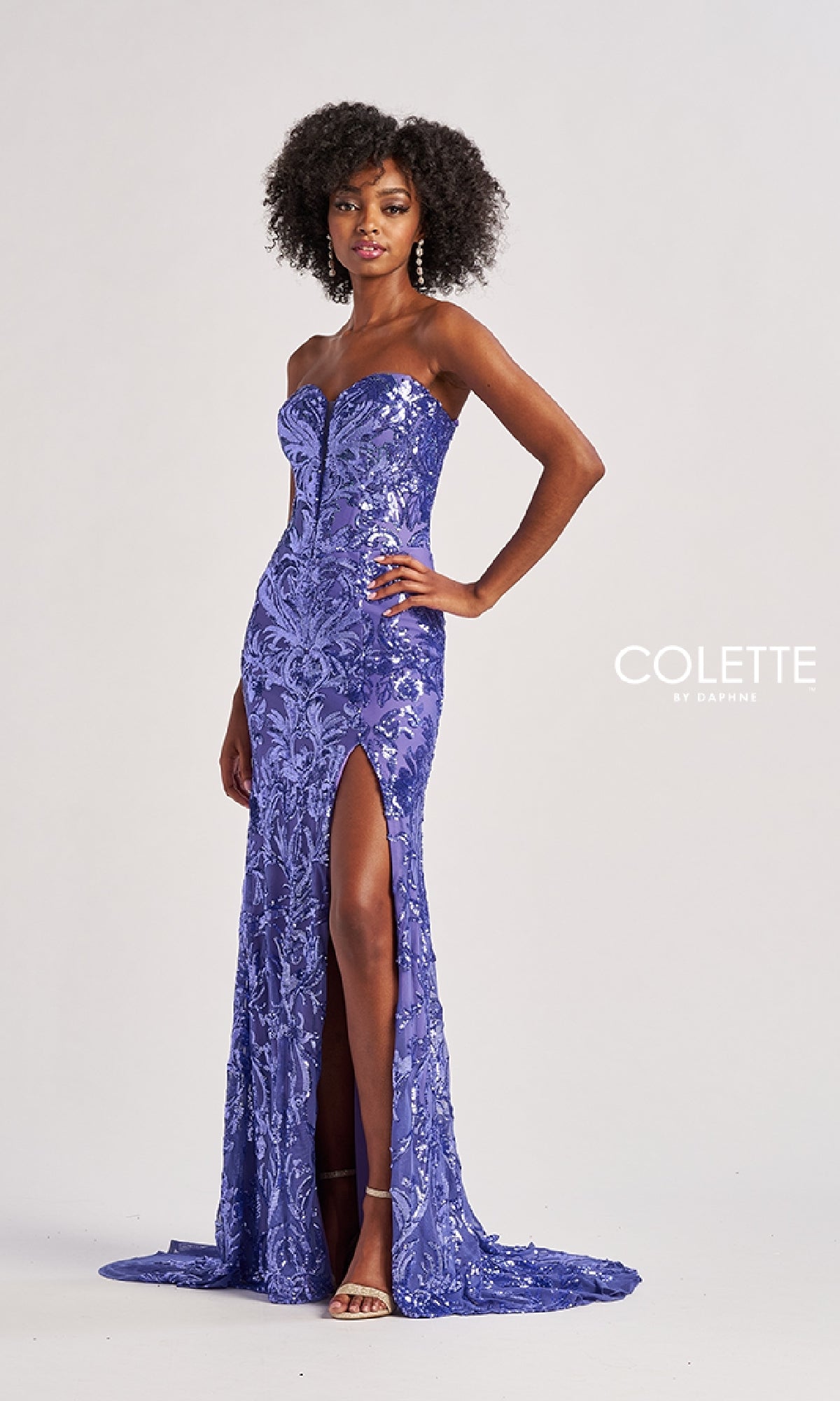 A woman wears the Colette CL8680 long prom dress—a floor-length, purple sequin gown with a thigh-high slit—posing elegantly against a plain background.